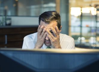 Man staring at his computer looking through his hands and holding his head, he looks worried