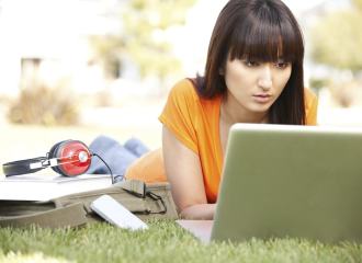 Lady lying in a park watching a video on a laptop