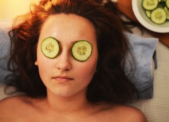 Woman laying on her back having a beauty spa treatment with sliced cucumbers over her eyes